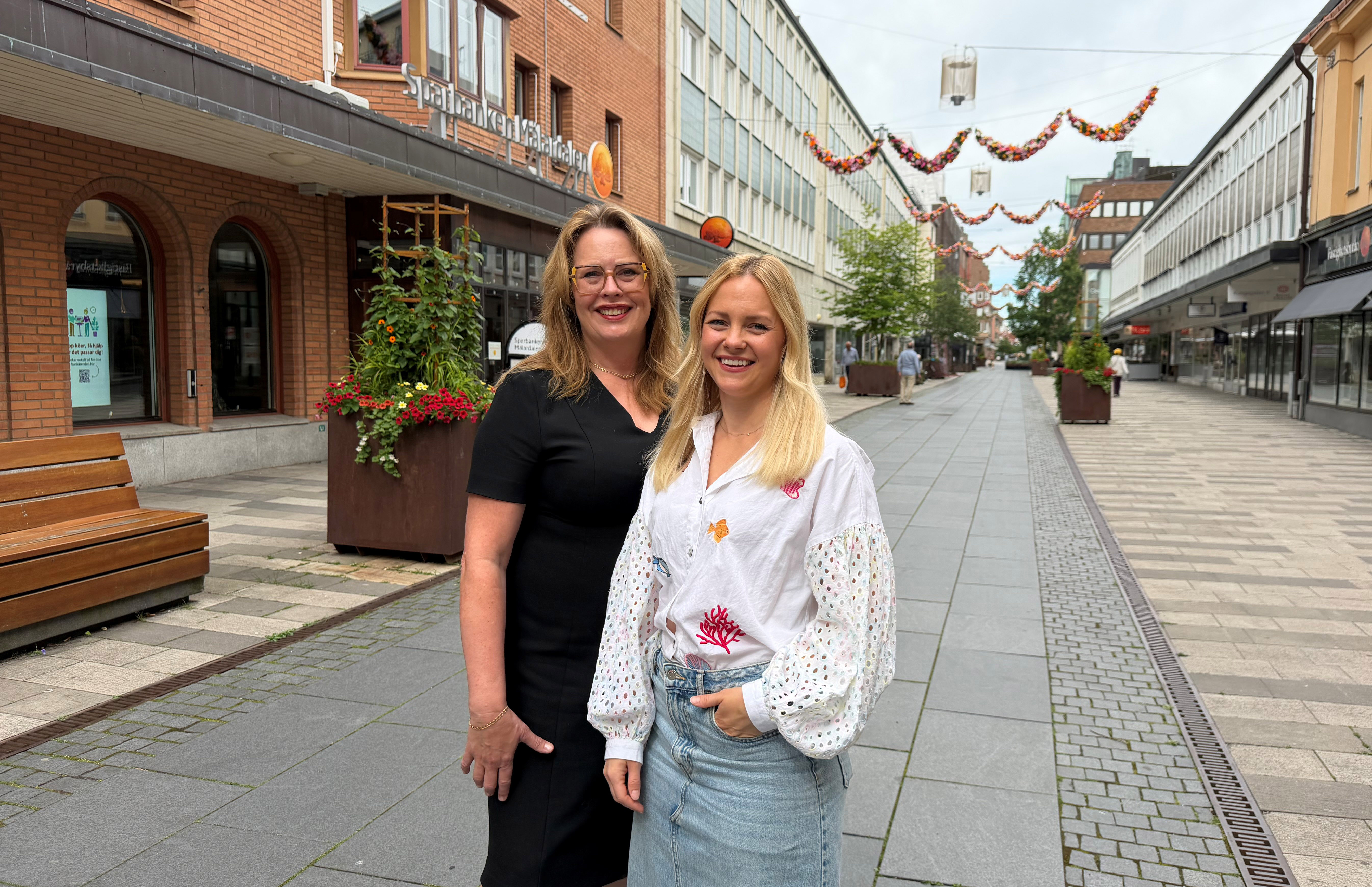 Två personer står på en gågata i stadsmiljö 